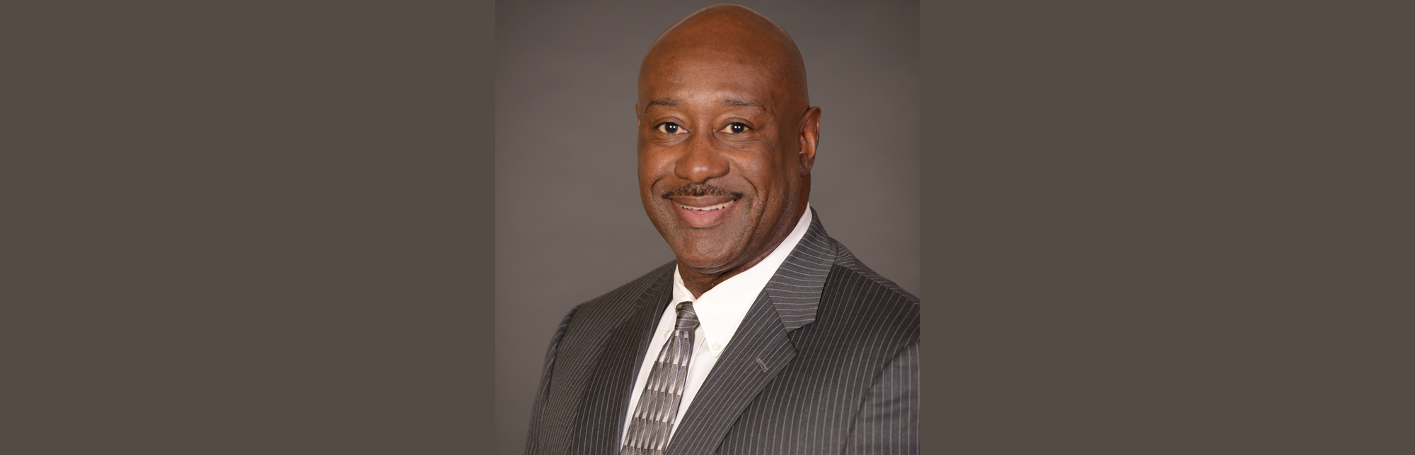 Professional man in a suit smiling against a gray background.